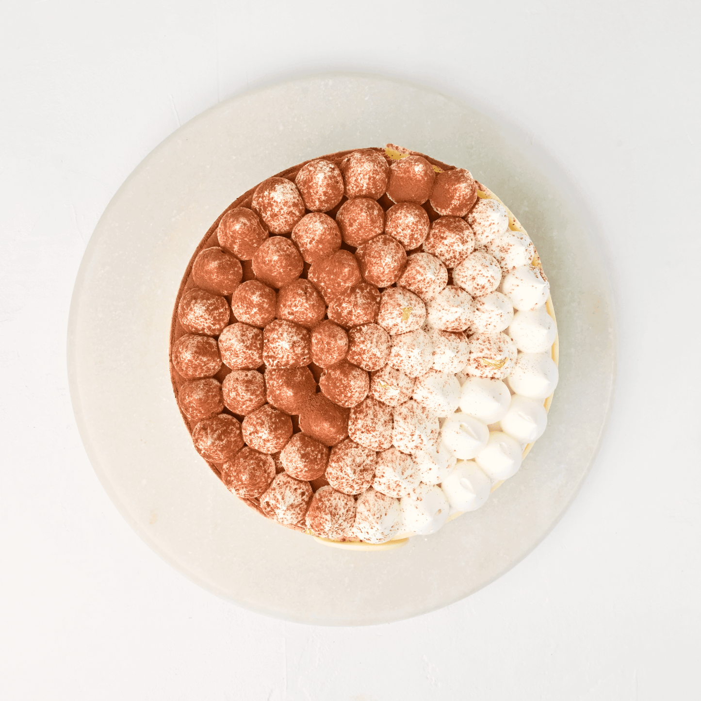 Lubov Tiramisu Celebration Cake on a serving stand with cocoa topping.