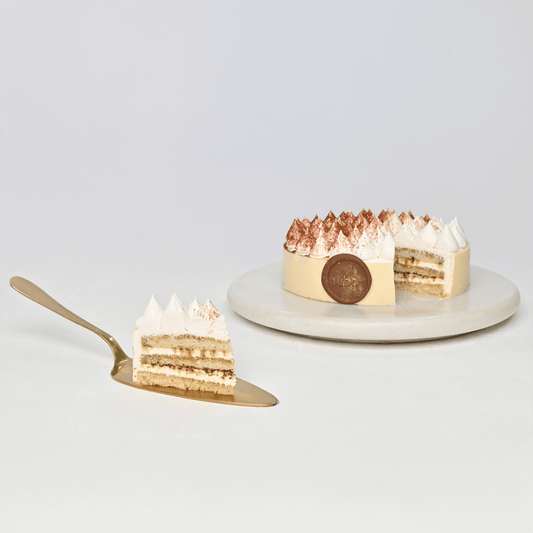 Lubov Tiramisu Celebration Cake on a serving stand with cocoa topping.